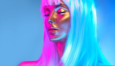 Glowing gold skin. Fashion model woman face in bright neon colourful lights, beautiful sexy woman with white hair and trendy make-up. Art design make up. Glittering, golden, metallic shine makeup