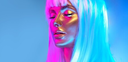 Glowing gold skin. Fashion model woman face in bright neon colourful lights, beautiful sexy woman with white hair and trendy make-up. Art design make up. Glittering, golden, metallic shine makeup